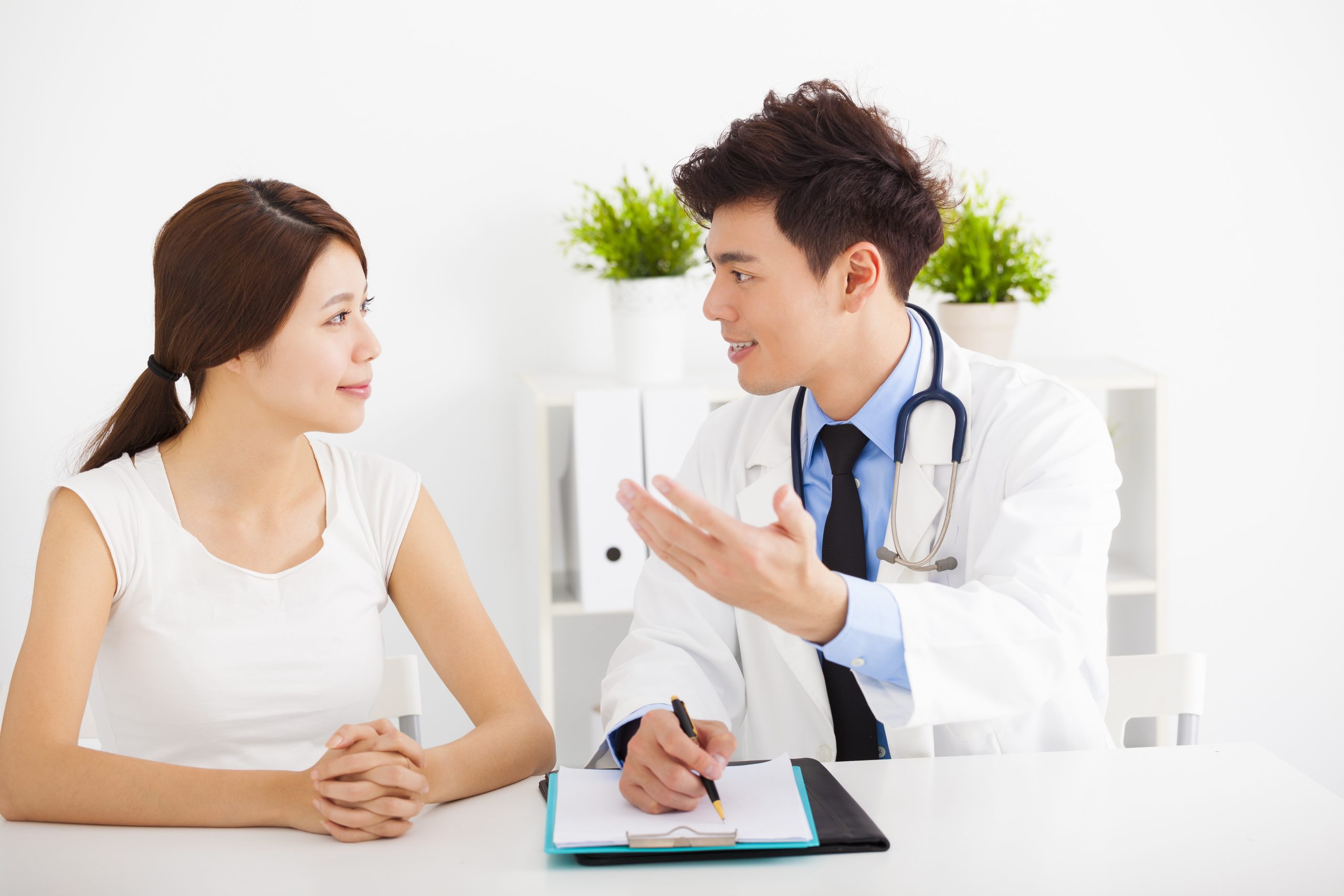 asian doctor talking with female patient in office